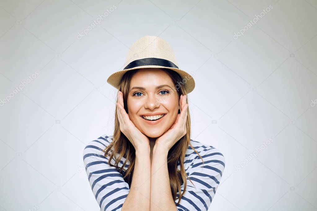 portrait of smiling woman wearing hat touching face on light background