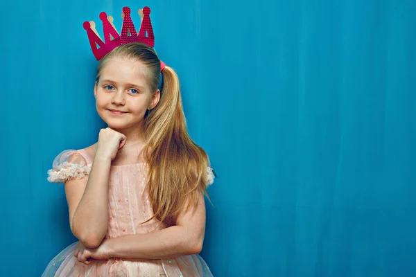 Lächelndes Mädchen in rosa Kleid steht vor blauer Wand. — Stockfoto