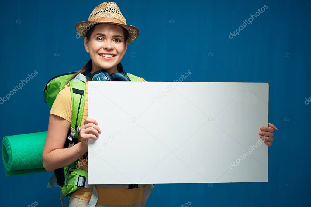 smiling woman tourist holding big white sign board on blue wall background