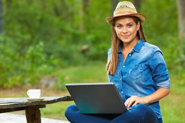 Bahçe laptop ve kahve Kupası ile tahta masada oturan genç kadın 