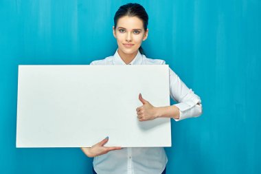 büyük beyaz tabela holding ve mavi duvar arka plan üzerinde başparmak gösterilmesini gülümseyen kadın