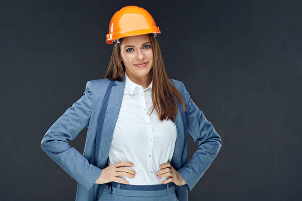 Smiling builder woman in safety helmet and white shirt and blue jacket standing on dark background