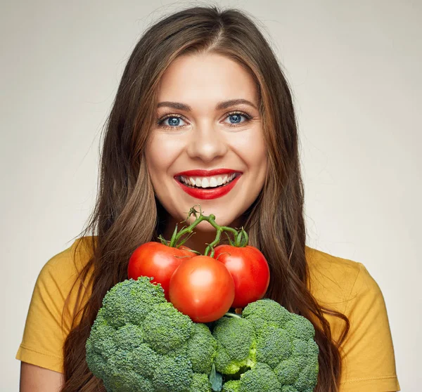 Smiling woman holding tomatoes and broccoli on beige background