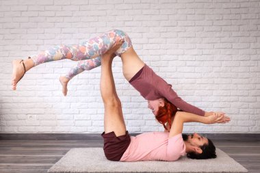 Genç çift evde farklı yerlerde akro yoga pozları vererek eğleniyor..