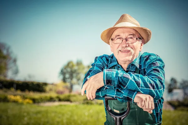 Retrato de um jardineiro sênior em pé em um jardim com uma pá . — Fotografia de Stock