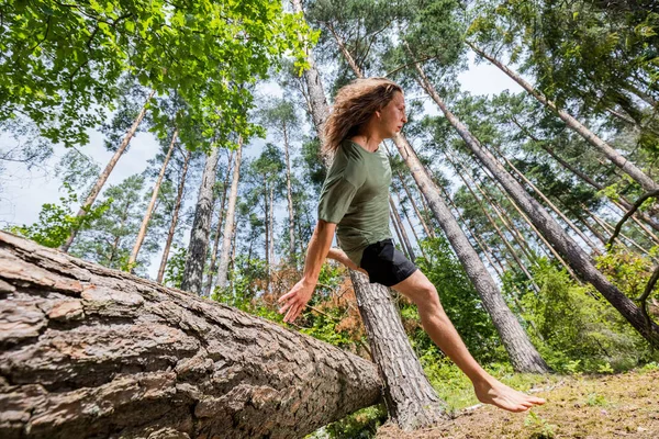 Junger Mann springt im Wald über Baumstamm. — Stockfoto