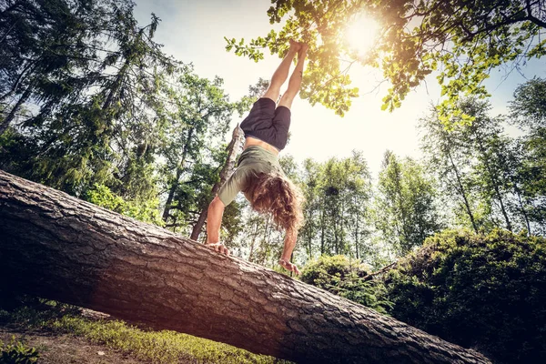 Ung man gör en handstand på en trädstam i skogen. — Stockfoto