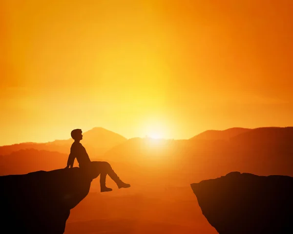 Hombre sentado relajado en el borde de la montaña mirando el horizonte panorámico del atardecer . —  Fotos de Stock