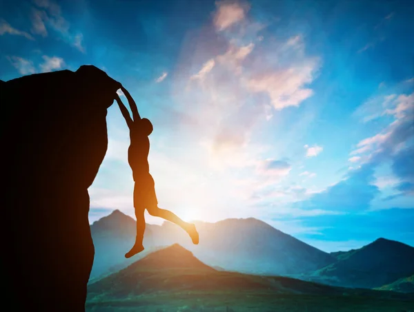 Man hanging on the edge of mountain at sunset — Stock Photo, Image