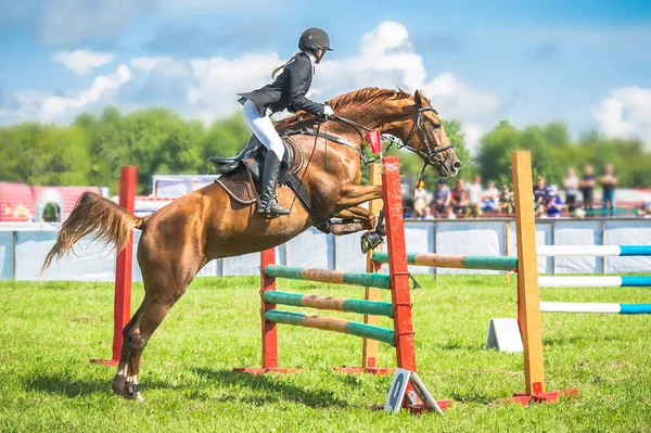 Jeune, femme jockey sur son cheval bondissant sur un obstacle . — Photo