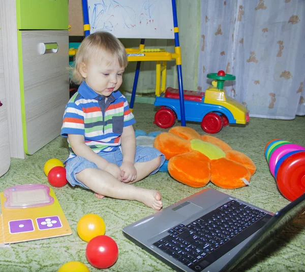 Lindo niño divertido bebé con pelo largo y rubio rizado jugando en la computadora y el teléfono móvil —  Fotos de Stock