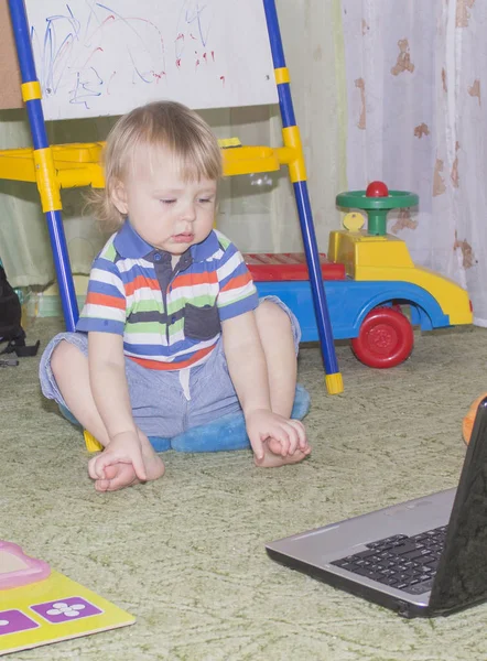 Lindo niño divertido bebé con pelo largo y rubio rizado jugando en la computadora y el teléfono móvil —  Fotos de Stock