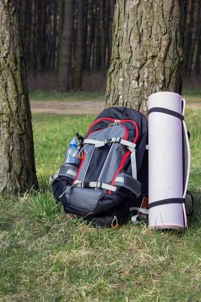 Trekking heavy backpack in forest with green jars of water.