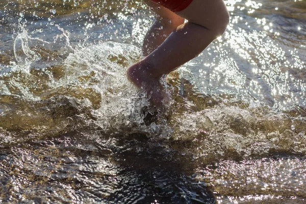 Füße, und eine Menge Wassertropfen, die auf dem Hintergrund des Strandes plätschern — Stockfoto