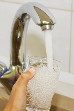 Mutfak musluğundan dökülen bir bardak suyu tutan el.