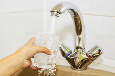 Mutfak musluğundan dökülen bir bardak suyu tutan el.