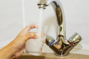 Mutfak musluğundan dökülen bir bardak suyu tutan el.