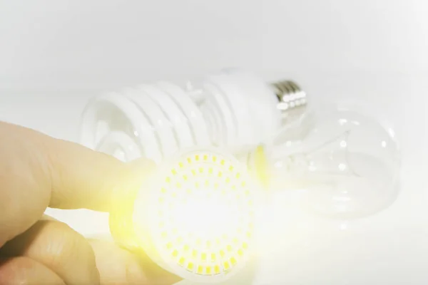 Несколько различных свинцовых ламп и компактные люминесцентные лампы и мужская рука на светлом фоне . — стоковое фото