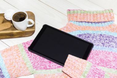 Bir tablet kişisel bilgisayar ahşap arka plan üzerinde bir parlak renkli kazak.