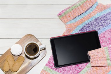 Bir tablet kişisel bilgisayar ahşap arka plan üzerinde bir parlak renkli kazak.