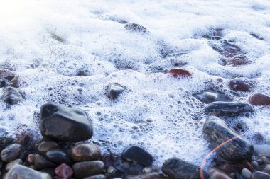 Islak, parlak, farklı renkte çakıl taşları ve deniz köpüğü..