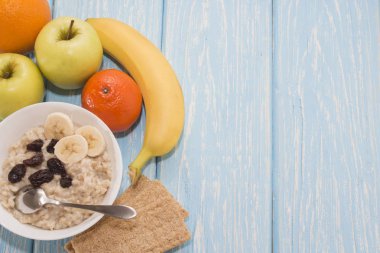 Sağlıklı kahvaltı. Beyaz kase kuru üzümlü yulaf ezmesi. İki yeşil elma, muz. Düz Üstten Görünüm.