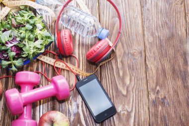 Ahşap bir tezgah, kopya alanı, diyet ve sağlıklı beslenme kavramı dumbbells ile taze organik sebze. Kulaklık ve telefon. Müzik spor