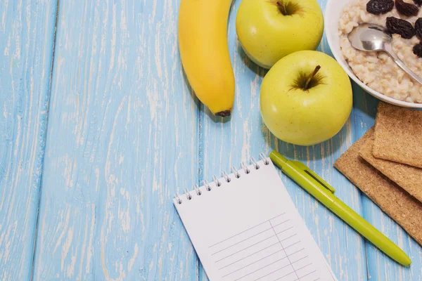 Sağlıklı kahvaltı. Beyaz kase kuru üzümlü yulaf ezmesi. İki yeşil elma, muz. Düz Üstten Görünüm.