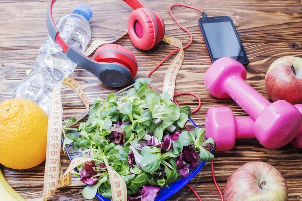 Ahşap bir tezgah, diyet ve sağlıklı beslenme kavramı dumbbells ile taze organik sebze. Kulaklık ve telefon. Müzik spor