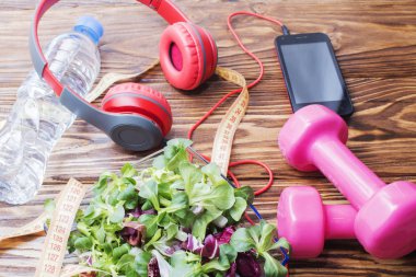 Ahşap bir tezgah, kopya alanı, diyet ve sağlıklı beslenme kavramı dumbbells ile taze organik sebze. Kulaklık ve telefon. Müzik spor