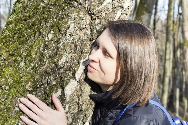 Meisje een enorme boomstam knuffelen in het Park, glimlachend in de camera. Het concept van bescherming van de natuur — Stockfoto