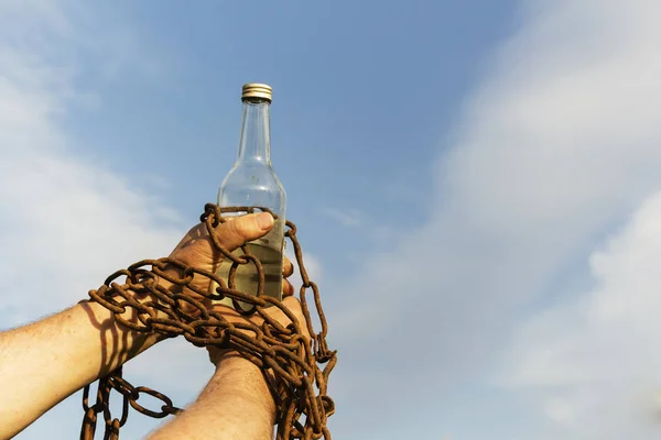 Incatenato a mano a una bottiglia di alcol, contro il cielo blu — Foto Stock