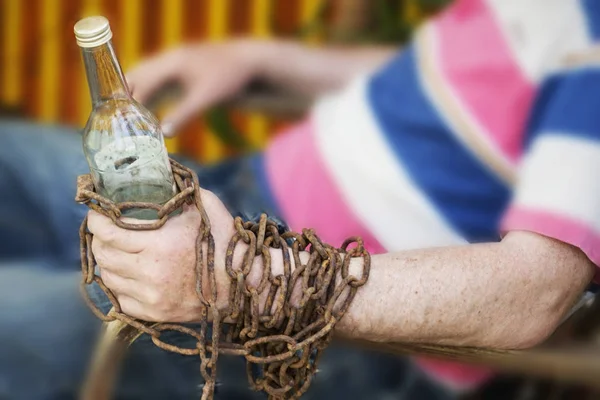 Incatenato a mano a una bottiglia di alcol, un uomo seduto su una sedia — Foto Stock