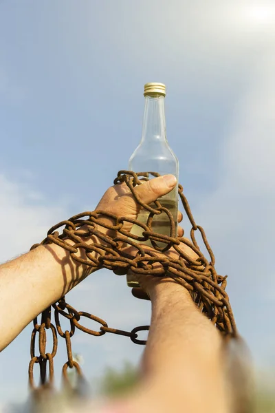 Incatenato a mano a una bottiglia di alcol, contro il cielo blu — Foto Stock