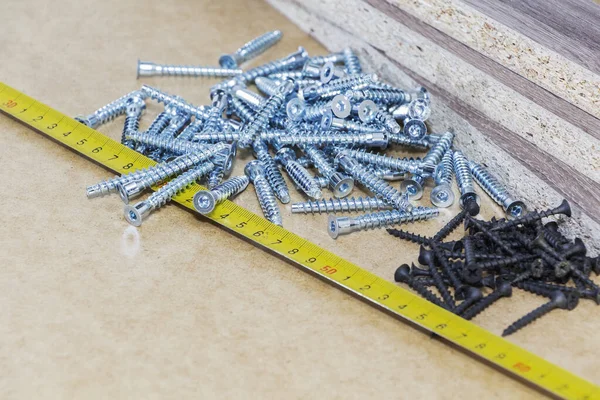 Screws, confirmations for furniture, tape measure, lie on the table. Furniture production