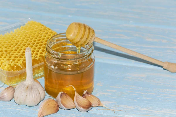 Honey and pieces of garlic on the background of honeycomb. Honey in a glass jar and honeycomb. — Stock Photo, Image
