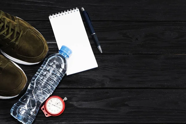 Baskets et une bouteille d'eau, un bloc-notes, un chronomètre, sur un fond en bois noir. Le concept d'un mode de vie sain — Photo