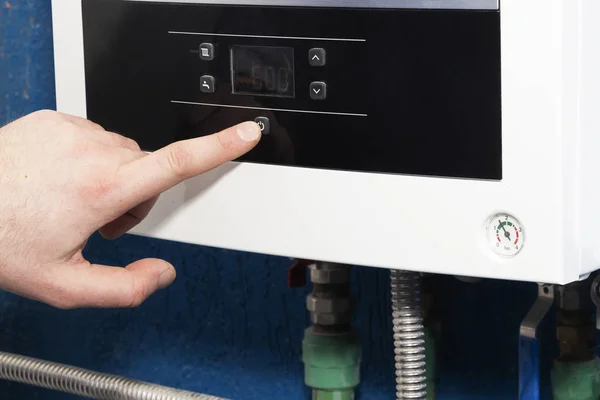 El dedo del hombre enciende o apaga el botón de arranque del sistema de calefacción en la sala de calderas. El concepto de calefacción doméstica en la temporada otoño-invierno . — Foto de Stock
