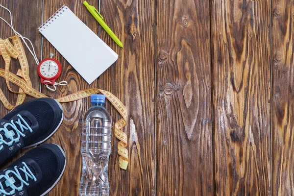 Здоровый образ жизни и спортивный фон. Спортивная обувь, Блокнот и ручка, секундомер и бутылка воды на деревянном фоне с копирайтом, вид сверху . — стоковое фото
