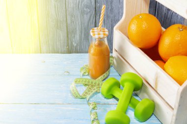 Bir sürü portakal, bir şişe meyve suyu, halterler, ahşap bir arka planda mezura. Fitness, spor beslenme.