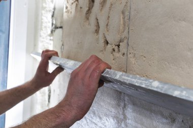 Duvarı elle kaplamak için uzun bir spatulası olan inşaat işçisi.