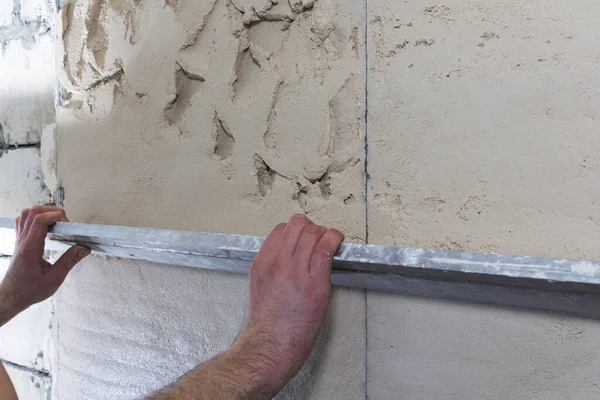 Construction worker with a long spatula to plaster the wall by hand