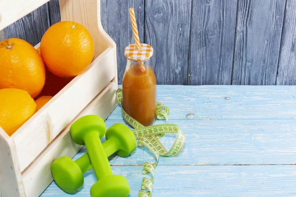 Много апельсинов и бутылка сока, гантели, измерительная лента на деревянном текстурированном фоне. Фитнес, спортивное питание . — стоковое фото