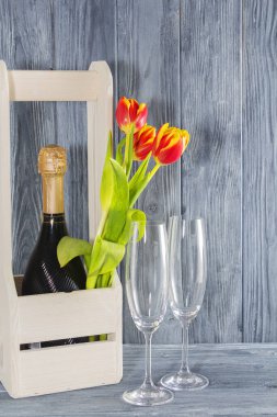 Tahta bir kutuda bir şişe şampanya. 2 bardak şampanya ve lale çiçeklerinin yanında. Tatil 8 Mart, Anneler Günü. Romantik ortam