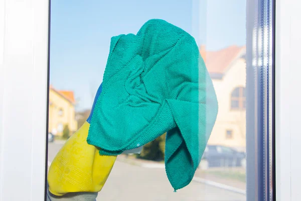 A hand in a yellow glove wipes the window with a rag against the background of low-rise buildings. — Stock Photo, Image