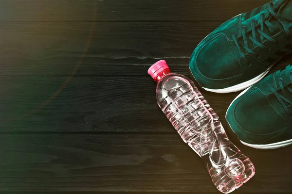 Zapatillas deportivas y una botella de agua sobre un fondo de madera negro. El concepto de un estilo de vida saludable —  Fotos de Stock