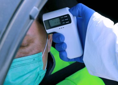 Doktor aracın sürücüsünün kontrol noktasında koronavirüs var mı diye vücut ısısını kontrol ediyor. Bir termometreyle. Yakın plan.