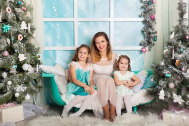 İki kız kardeş ve bir genç anne Noel süslemeli bir stüdyoda pastel renklerde.