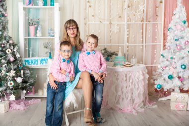 Pastel renklerde Noel süslemeli bir stüdyoda iki erkek kardeş ve genç anne.