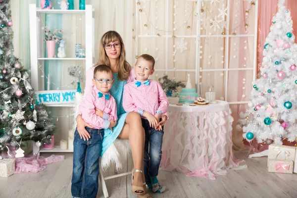 Pastel renklerde Noel süslemeli bir stüdyoda iki erkek kardeş ve genç anne.